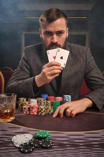 good-looking-bearded-guy-classic-suit-is-playing-poker-sitting-table-casino-smoke-he-is-showing-two-aces-camera-realising-that-has-won-gambling-money-games-min